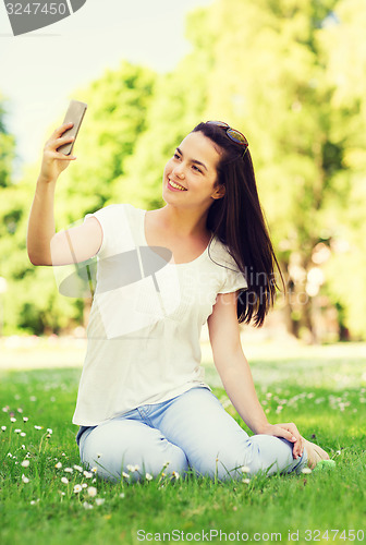 Image of smiling young girl with smartphone sitting in park