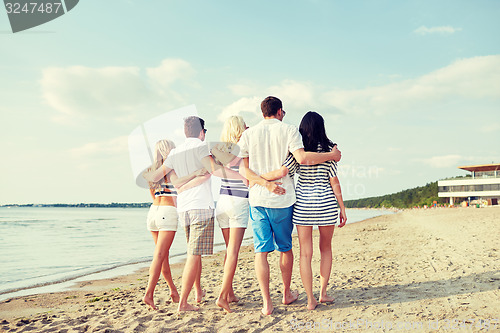 Image of smiling friends hugging and walking on beach