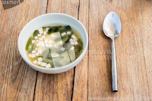 Image of bowl of soup with tofu cheese and spoon on table