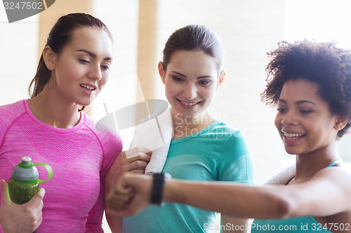 Image of happy women showing time on wrist watch in gym