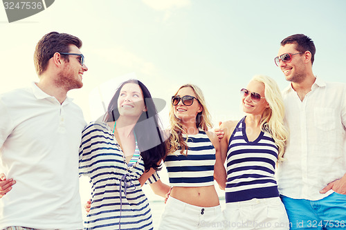 Image of smiling friends in sunglasses talking on beach