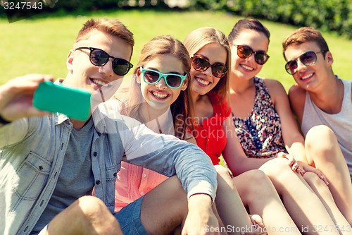 Image of smiling friends with smartphone sitting on grass