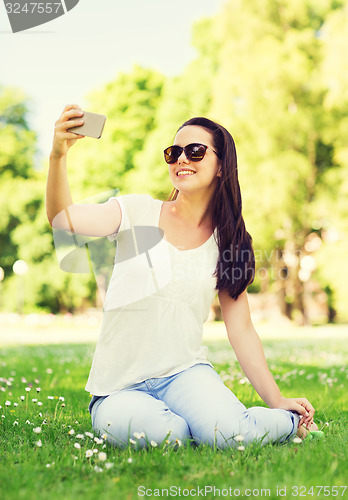 Image of smiling young girl with smartphone sitting in park