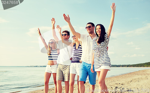 Image of smiling friends walking on beach and waving hands