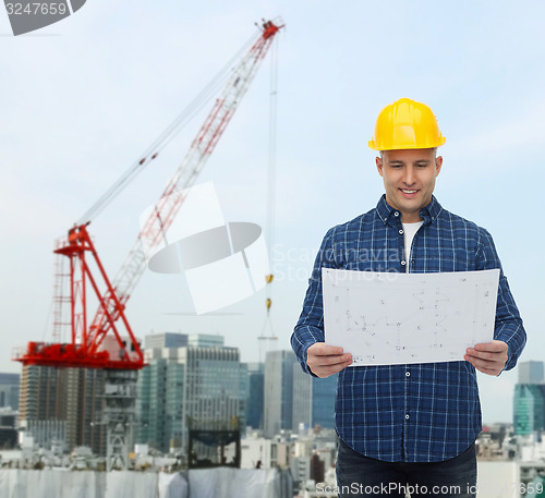 Image of smiling male builder in helmet with blueprint