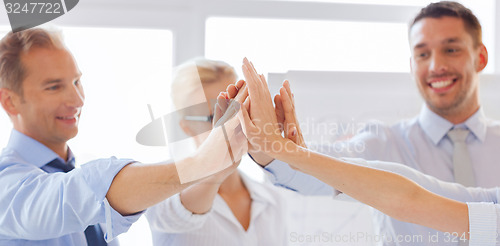 Image of happy business team giving high five in office