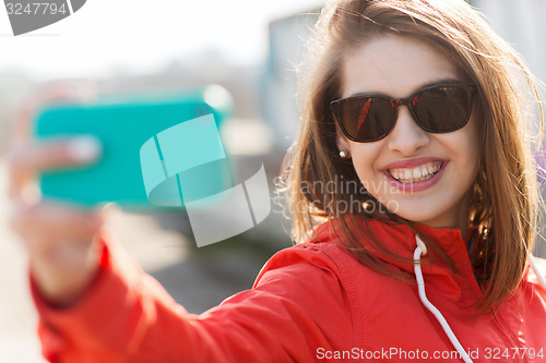 Image of smiling young woman taking selfie with smartphone