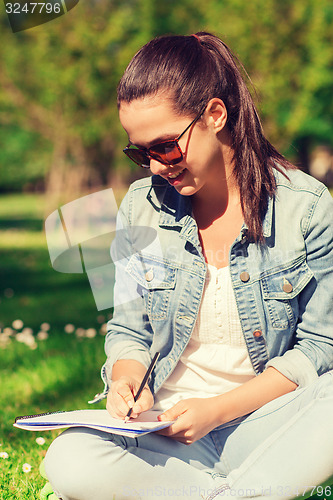 Image of smiling young girl with notebook writing in park