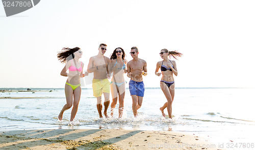 Image of smiling friends in sunglasses running on beach