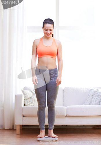 Image of happy young woman weighing on scales at home