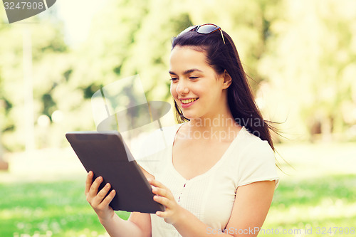 Image of smiling young girl with tablet pc sitting on grass