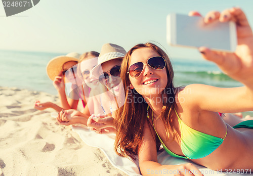 Image of group of smiling women with smartphone on beach