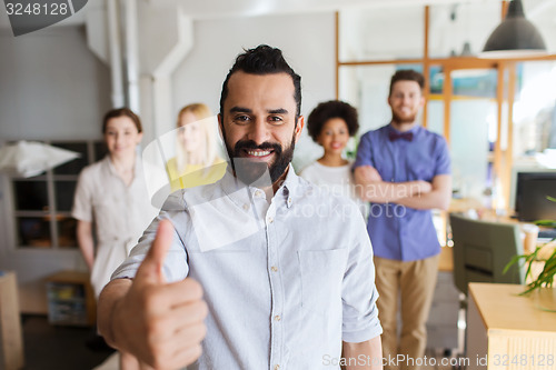 Image of happy creative team showing thumbs up in office