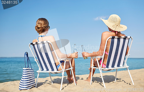 Image of happy women sunbathing in lounges on beach