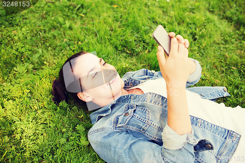 Image of smiling young girl with smartphone lying on grass
