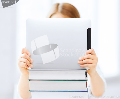 Image of girl hiding behind tablet pc and books at school