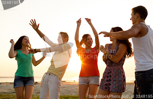 Image of smiling friends dancing on summer beach