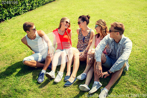 Image of group of smiling friends outdoors sitting in park