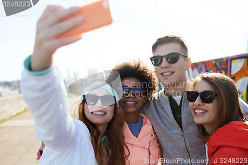 Image of smiling friends taking selfie with smartphone