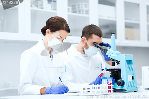 Image of scientists with clipboard and microscope in lab