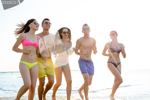 Image of smiling friends in sunglasses running on beach