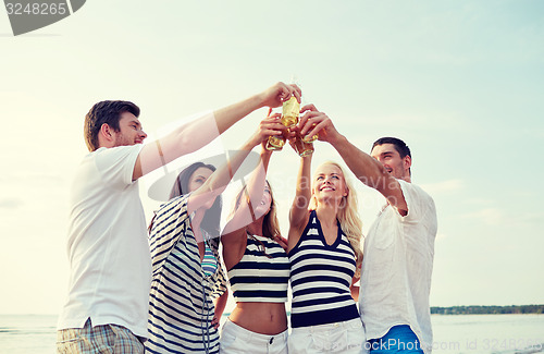 Image of smiling friends clinking bottles on beach