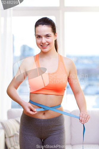 Image of happy sporty woman measuring her waist with tape