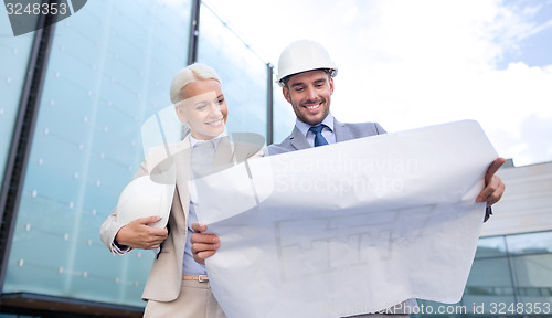 Image of smiling businessmen with blueprint and helmets