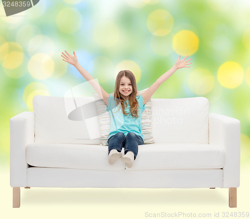 Image of happy girl sitting on sofa with raised hands