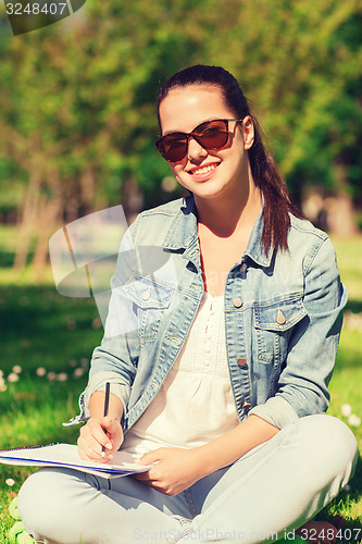 Image of smiling young girl with notebook writing in park