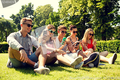 Image of smiling friends with smartphones sitting on grass