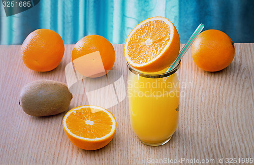 Image of Orange juice in a glass and oranges on the table.