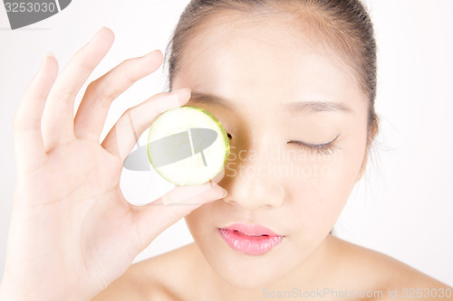 Image of Beautiful young Asian girl holding cucumber slice over face