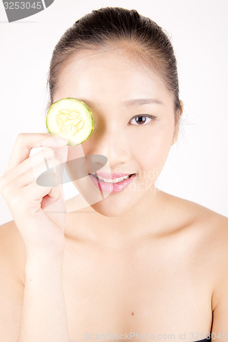 Image of Beautiful young Asian girl holding cucumber slice over face