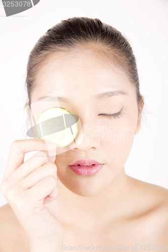 Image of Beautiful young Asian girl holding cucumber slice over face