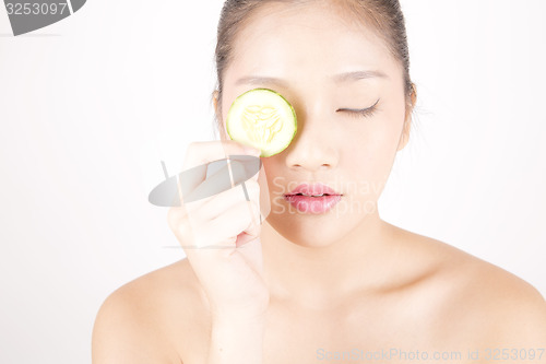 Image of Beautiful young Asian girl holding cucumber slice over face