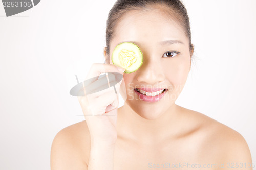 Image of Beautiful young Asian girl holding cucumber slice over face