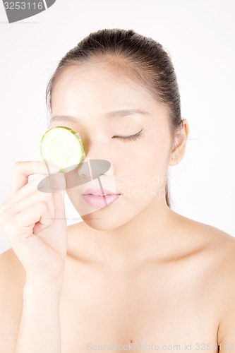 Image of Beautiful young Asian girl holding cucumber slice over face