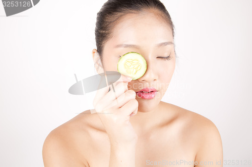 Image of Beautiful young Asian girl holding cucumber slice over face