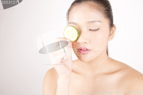 Image of Beautiful young Asian girl holding cucumber slice over face