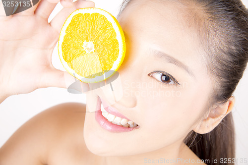 Image of Beautiful young Asian girl holding orange slice over face