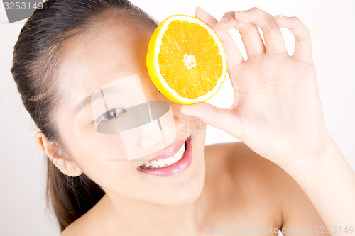 Image of Beautiful young Asian girl holding orange slice over face