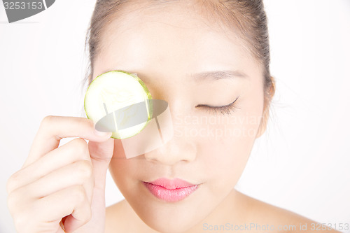 Image of Beautiful young Asian girl holding cucumber slice over face