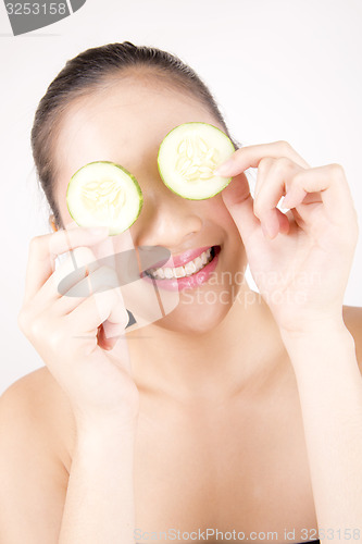 Image of Beautiful young Asian girl holding cucumber slice over face