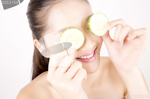 Image of Beautiful young Asian girl holding cucumber slice over face