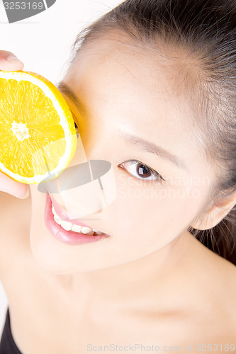 Image of Beautiful young Asian girl holding orange slice over face