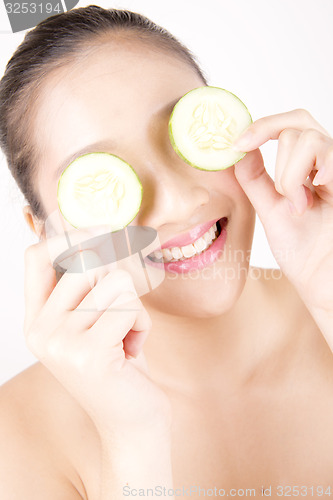 Image of Beautiful young Asian girl holding cucumber slice over face