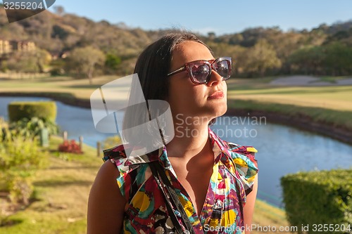 Image of Young woman in sunglasses enjoying summer breeze at beach. 