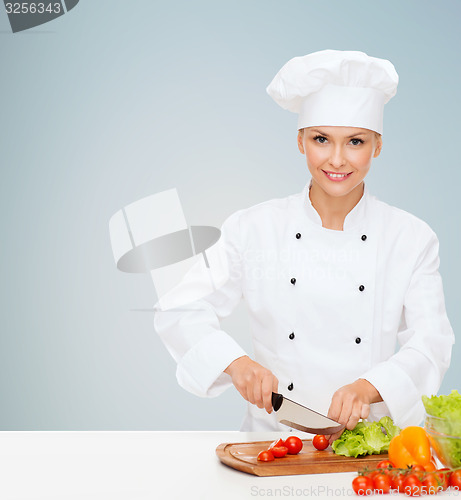 Image of smiling female chef chopping vegetables