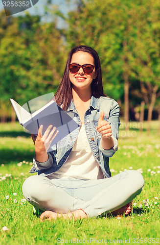 Image of smiling young girl with book sitting on grass